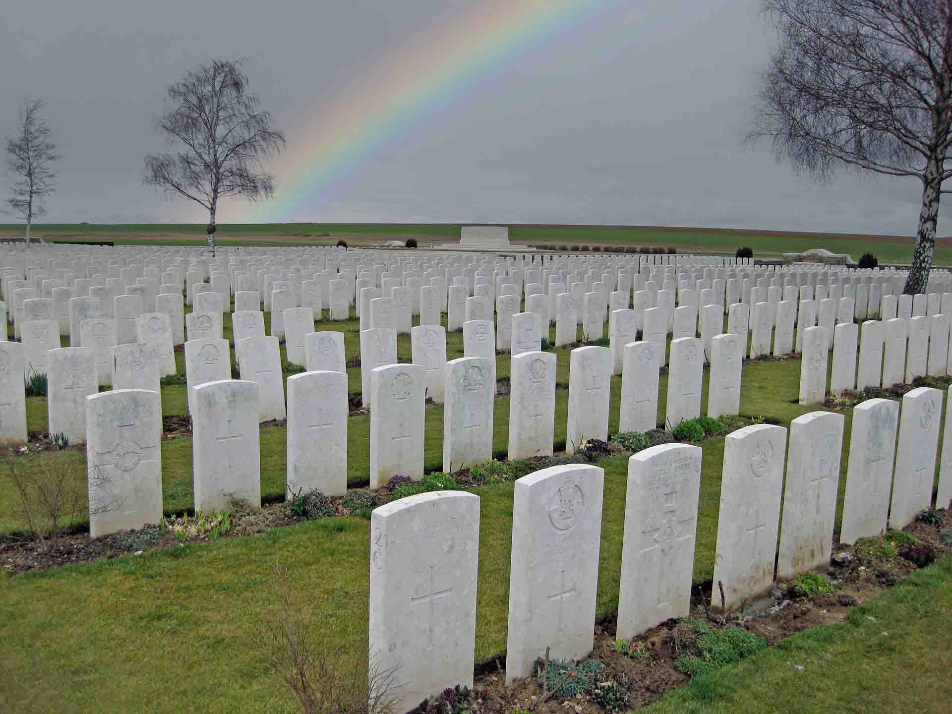 War Cemetery With White Headstones And Rainbow In The Sky.